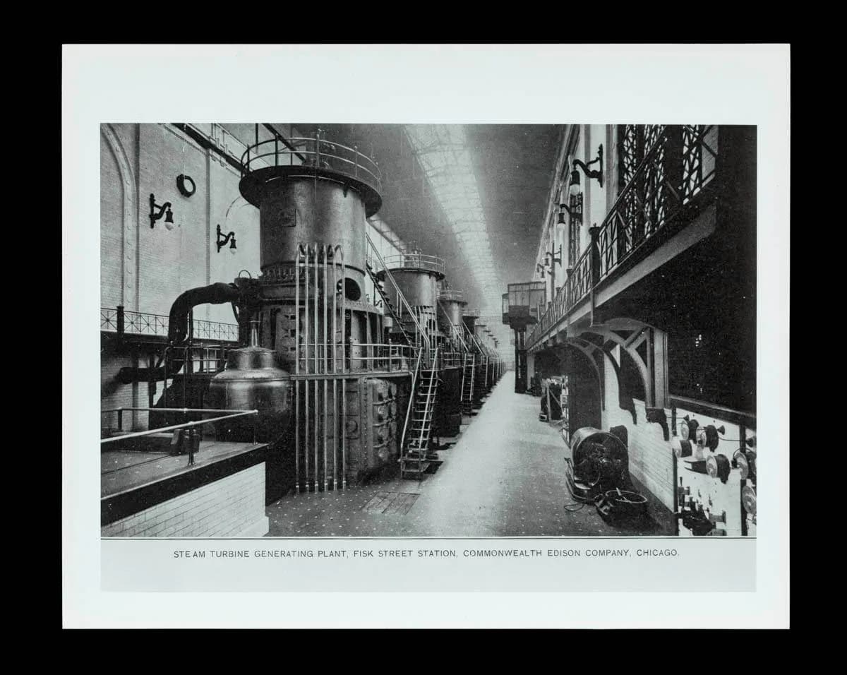 Black-and-white photograph of a long industrial turbine hall with large cylindrical generators, captioned Steam Turbine Generating Plant, Fisk Street Station, Commonwealth Edison Company, Chicago.