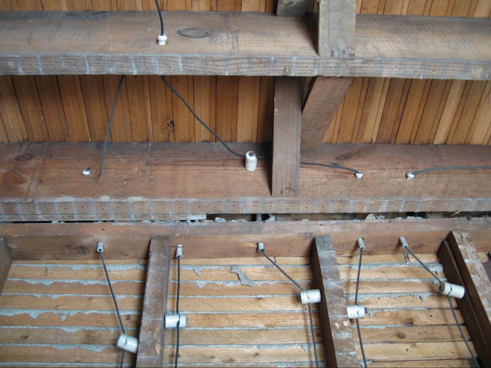 Color photograph of exposed wood ceiling joists with bare wires threaded through white porcelain knob-and-tube insulators.